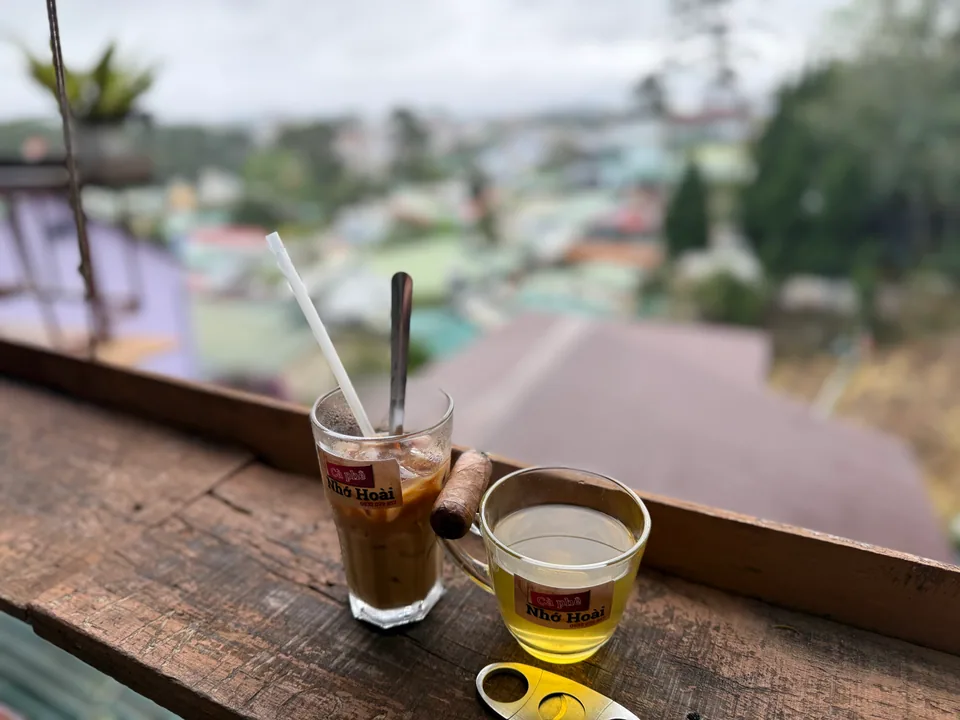 Toàn cảnh không gian quán — tủ kính tiệm may cũ, đèn vàng và bàn gỗ